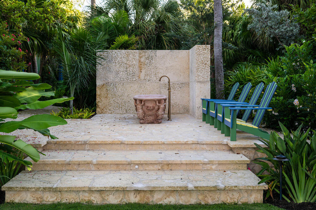 Stone patio with chairs and lush greenery.